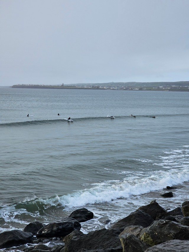 Multiple surfers paddling for the same hip high wave